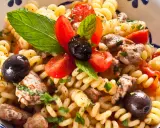 Pasta con pesce spada, pomodorini, olive nere e menta fresca in una ciotola decorata.