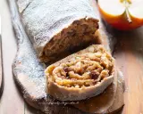 Delizioso strudel di mele con pasta sfoglia, cosparso di zucchero a velo, su un tagliere di legno.