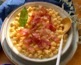 Un piatto fumante di pasta e ceci, arricchito da fette di prosciutto crudo e una foglia di alloro.
