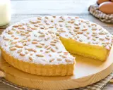 Una deliziosa torta della nonna, con crema gialla, ricoperta di pinoli e zucchero a velo, pronta per essere gustata.