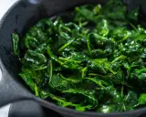Spinaci freschi e lucidi che sfrigolano in una padella di ghisa, pronti per essere gustati.