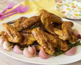 Alette di pollo in padella, dorate e succulente, servite con cipolle rosse e asparagi su un piatto bianco.