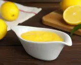 Una ciotola bianca contiene una vellutata crema al limone, con limoni freschi sullo sfondo.