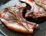 Due braciole di maiale succulente cuociono in padella con rametti di rosmarino.