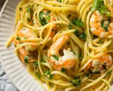 Un piatto invitante di pasta con gamberetti, condita con prezzemolo fresco e servita su un piatto bianco.