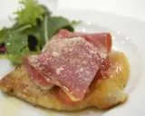 Cotoletta alla bolognese dorata, coperta da prosciutto crudo e parmigiano, con un contorno di insalata fresca.