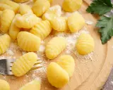 Gnocchi fatti in casa pronti per la friggitrice ad aria, spolverati di farina su un tagliere di legno.