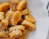 Gnocchi di zucca dorati, conditi con burro fuso, pepe nero e scaglie di parmigiano, pronti per essere gustati.