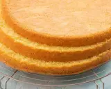 Tre soffici strati di pan di spagna senza glutine raffreddano su una griglia. Un'etichetta con scritto "senza glutine" è appesa alla griglia.