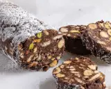 Salame di cioccolato senza uova, ricco di nocciole, mandorle e pistacchi, spolverato di zucchero a velo.