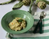 Un cremoso risotto con carciofi freschi, guarnito con una fogliolina di menta, pronto per essere gustato.