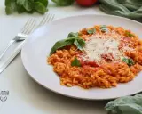 Un cremoso risotto al pomodoro, guarnito con basilico fresco e parmigiano grattugiato, pronto per essere gustato.