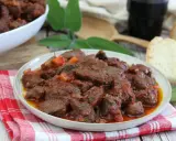 Cinghiale in umido fatto in casa da Benedetta, un piatto ricco e saporito, servito con pane fresco e un bicchiere di vino rosso.
