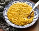Un cremoso risotto alla zucca, servito su un piatto decorato, con una forchetta che affonda nel piatto.