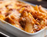 Un invitante piatto di pasta pasticciata al forno, con penne ricoperte da un ricco sugo e formaggio filante, pronto per essere gustato.
