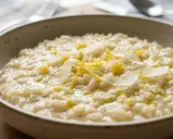 Un cremoso risotto al limone, guarnito con scorza di limone e scaglie di parmigiano, servito in una ciotola rustica.