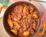 Un saporito spezzatino con patate, cotto lentamente in un tegame arancione, pronto per essere gustato.