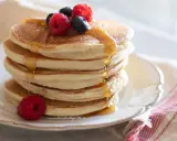 Pancakes senza glutine dorati, impilati e inzuppati di sciroppo, guarniti con lamponi e mirtilli freschi.