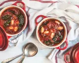 Due ciotole rosse con zuppa di cavolo nero e fagioli, pronte per essere gustate.