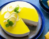 Delizioso cheesecake al limone con glassa gialla brillante, decorato con fette di limone e menta. Una fetta è stata tolta, rivelando la base croccante.