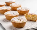 Deliziosi budini di riso in crostatina, spolverati di zucchero a velo. Uno è stato morso, rivelando il ripieno cremoso.