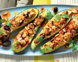 Zucchine ripiene vegetariane, dorate e gustose, guarnite con pinoli, olive e erbe fresche. Un piatto invitante e colorato.