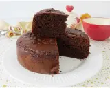 Una fetta di torta yogurt e cioccolato, soffice e golosa, è appoggiata su una torta intera. Sullo sfondo, una tazza rossa e un barattolo decorato.