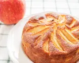 Torta di mele con yogurt, dorata e soffice, con mele a vista. Accanto, una mela rossa fresca.