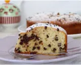 Una fetta di torta soffice con tante gocce di cioccolato, cosparsa di zucchero a velo, su un piatto lilla con una forchetta.