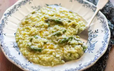 Un cremoso risotto con asparagi, servito in un piatto decorato. Un piatto primaverile che profuma di buono.