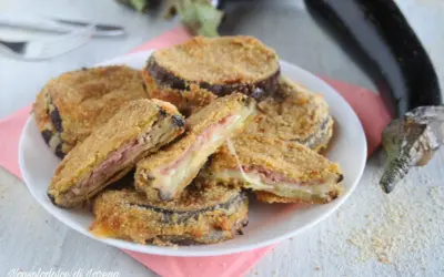 Cordon bleu di melanzane impanati e fritti, ripieni di prosciutto e formaggio filante, serviti su un piatto bianco.