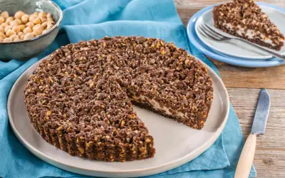 Sbriciolata ricotta e cioccolato con croccante copertura di nocciole. Una fetta è già servita su un piattino.