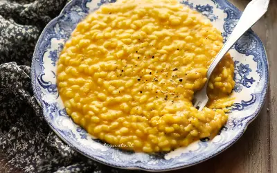 Un cremoso risotto alla zucca, servito su un piatto decorato, con una forchetta che affonda nel piatto.