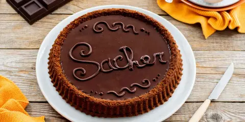 Una crostata morbida al cioccolato, decorata con la scritta "Sacher" in glassa, pronta per essere gustata.