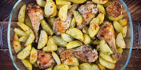 Delizioso pollo al forno con patate, erbe aromatiche e spicchi d'aglio arrostiti, servito in una teglia di vetro.