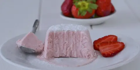 Delizioso semifreddo alle fragole, con una fetta servita su un cucchiaino e guarnito con zucchero a velo e fragole fresche.