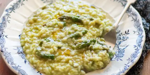 Un cremoso risotto con asparagi, servito in un piatto decorato. Un piatto primaverile che profuma di buono.