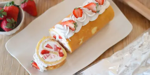 Rotolo panna e fragole decorato con panna montata e fragole fresche, pronto per essere gustato.