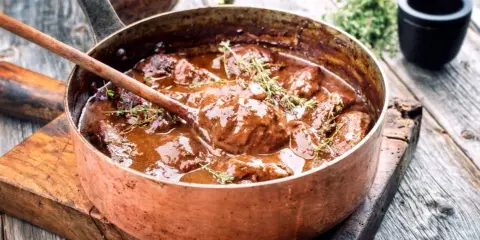 Un saporito brasato di manzo, cotto lentamente in una pentola di rame, guarnito con timo fresco.