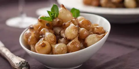 Ciotola di cipolle in agrodolce caramellate, guarnite con menta fresca.
