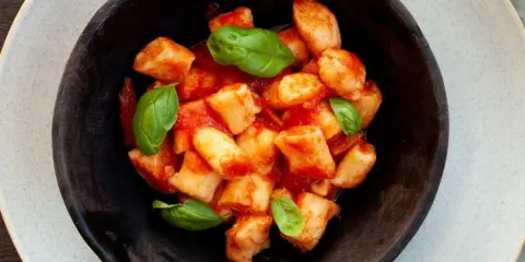 Gnocchi di ricotta soffici e saporiti, conditi con un sugo di pomodoro fresco e guarniti con foglie di basilico.