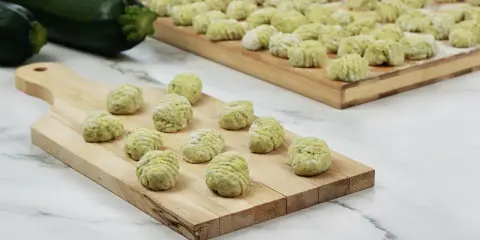 Gnocchi di zucchine freschi, pronti per essere cotti, disposti su taglieri di legno.