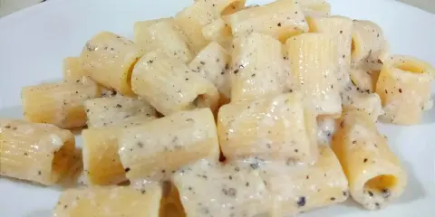 Piatto di rigatoni cremosi conditi con un classico cacio e pepe, pronti per essere gustati.