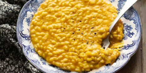 Un cremoso risotto alla zucca, servito su un piatto decorato, con una forchetta che affonda nel piatto.