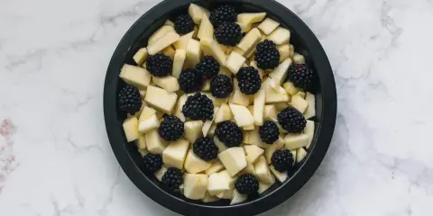 Mele a cubetti e more in una teglia nera, pronte per un delizioso crumble di mele.