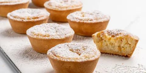 Deliziosi budini di riso in crostatina, spolverati di zucchero a velo. Uno è stato morso, rivelando il ripieno cremoso.