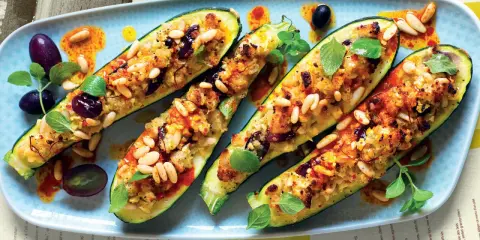 Zucchine ripiene vegetariane, dorate e gustose, guarnite con pinoli, olive e erbe fresche. Un piatto invitante e colorato.