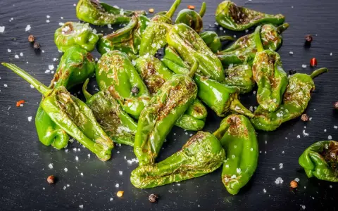 Friggitelli verdi, cotti in friggitrice ad aria, cosparsi di sale grosso e pepe nero su una superficie scura.