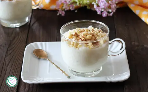 Una tazza di cremosa crema di riso, guarnita con mandorle tritate e cannella, pronta per essere gustata.