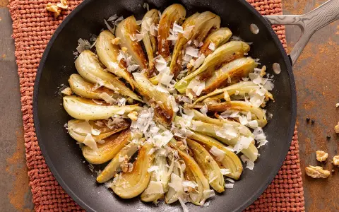 Finoçchi gratinati in padella, dorati e saporiti, guarniti con scaglie di formaggio e noci croccanti.